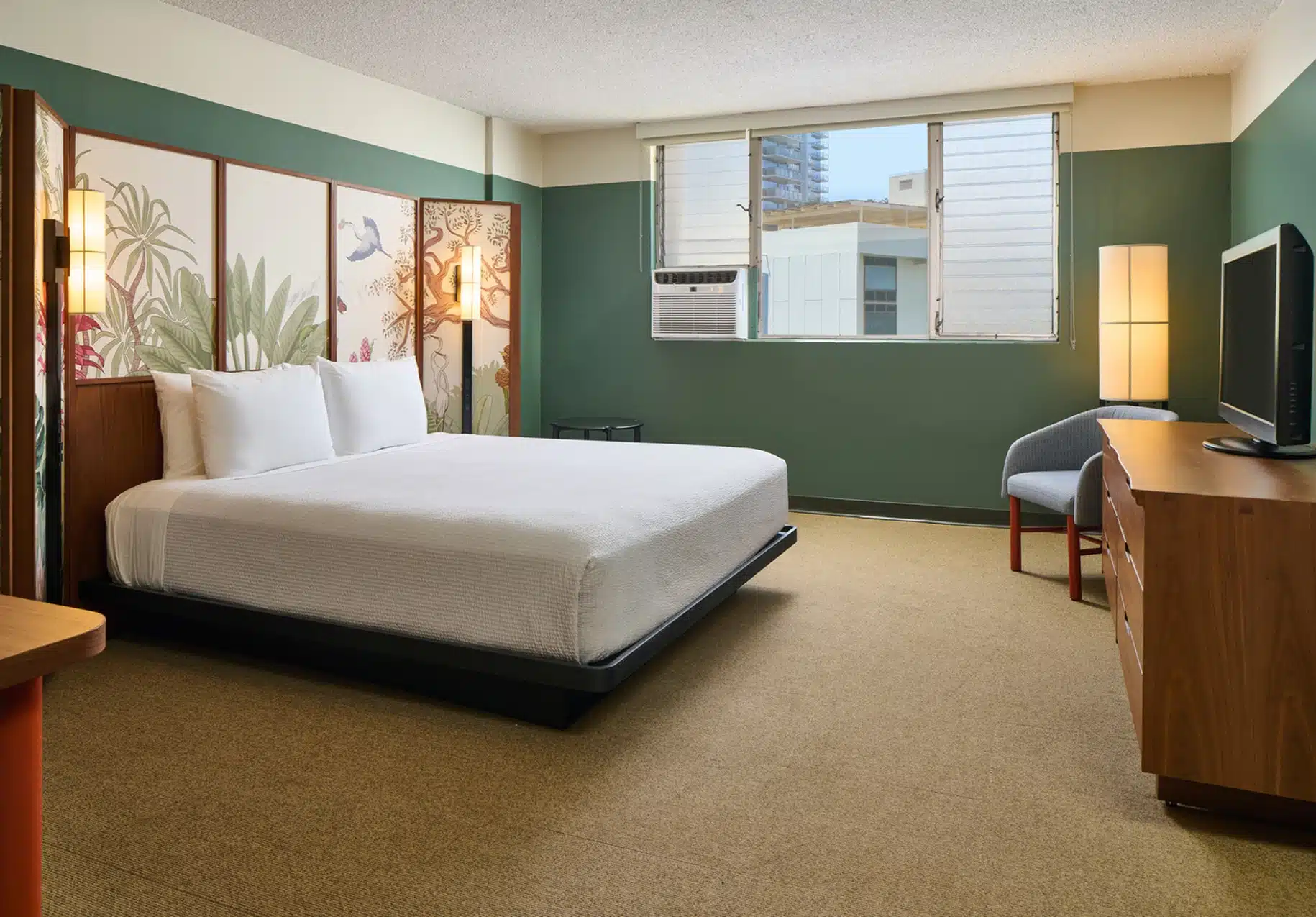 Hotel room with a king bed, botanical wall art, and a window facing city buildings