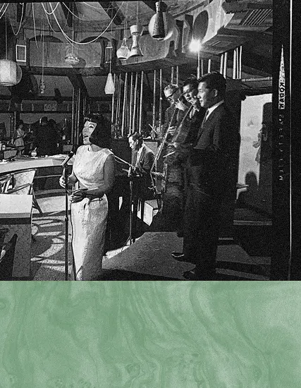 Vintage black-and-white scene of people singing at a restaurant bar