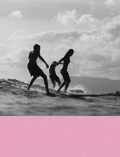 Silhouetted surfers walking through shallow water at sunset with a pink overlay