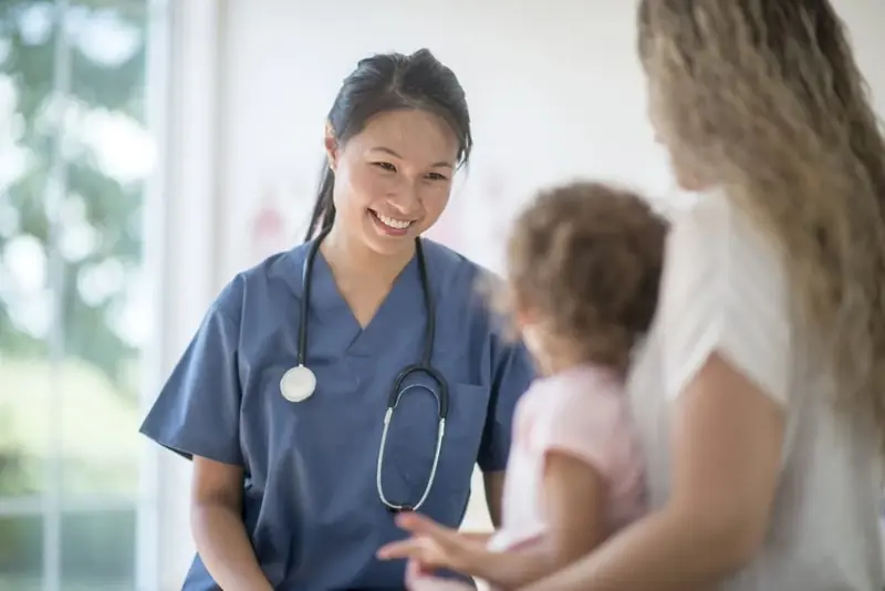 Nurse smiling while speaking with a mother holding a young child
