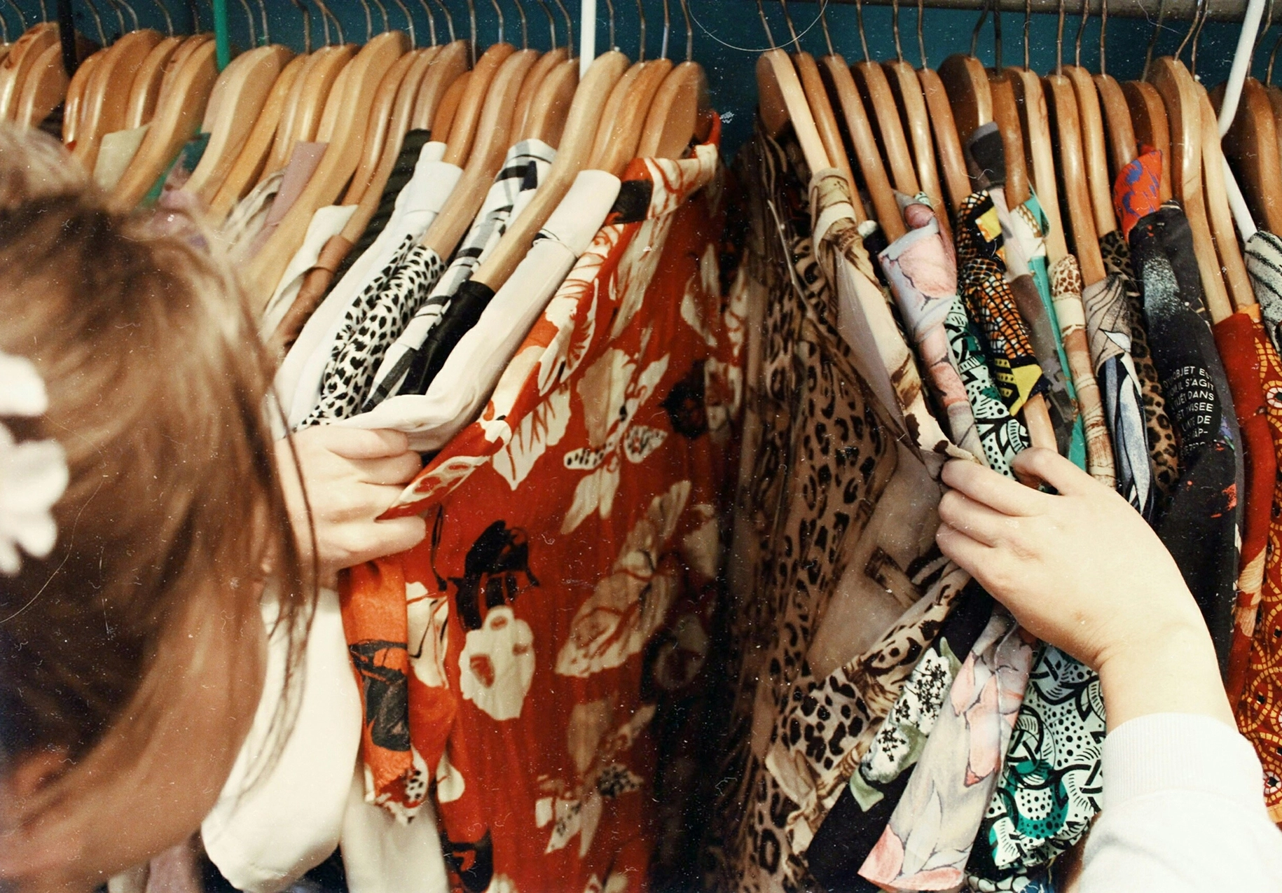 Person browsing patterned clothing on wooden hangers