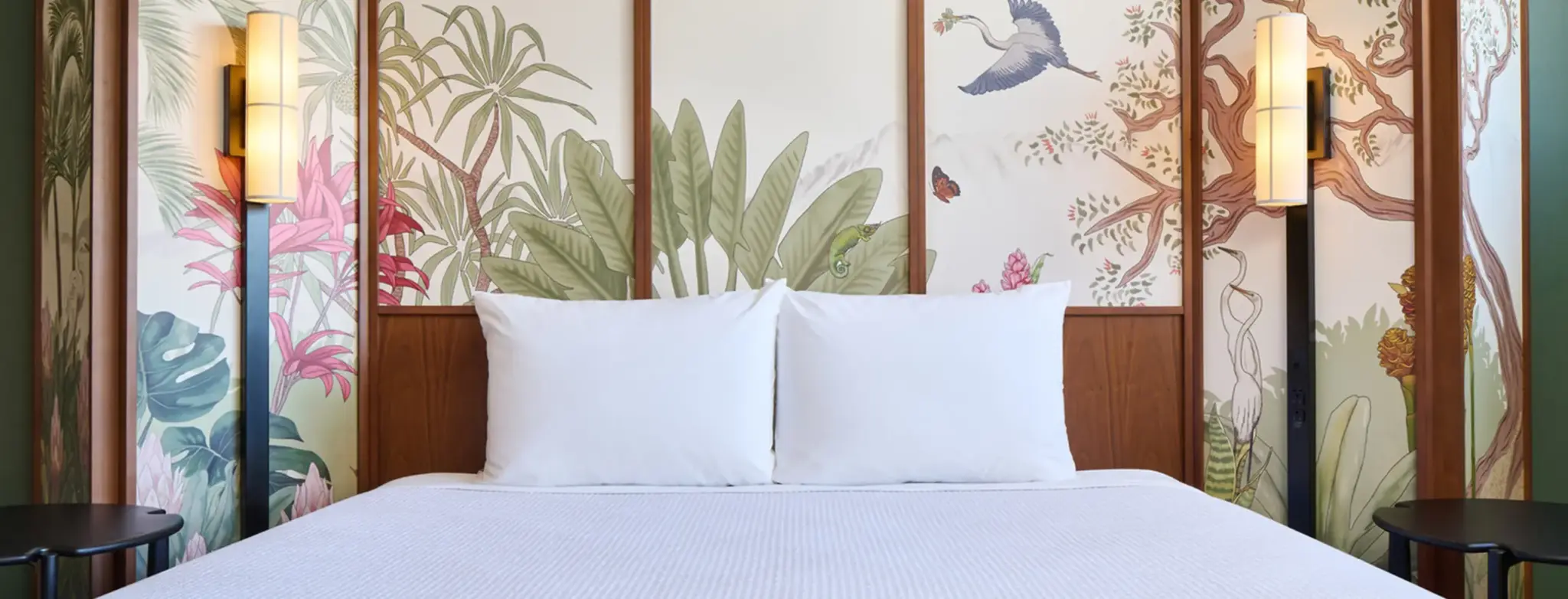 Bed with white pillows set against a botanical mural