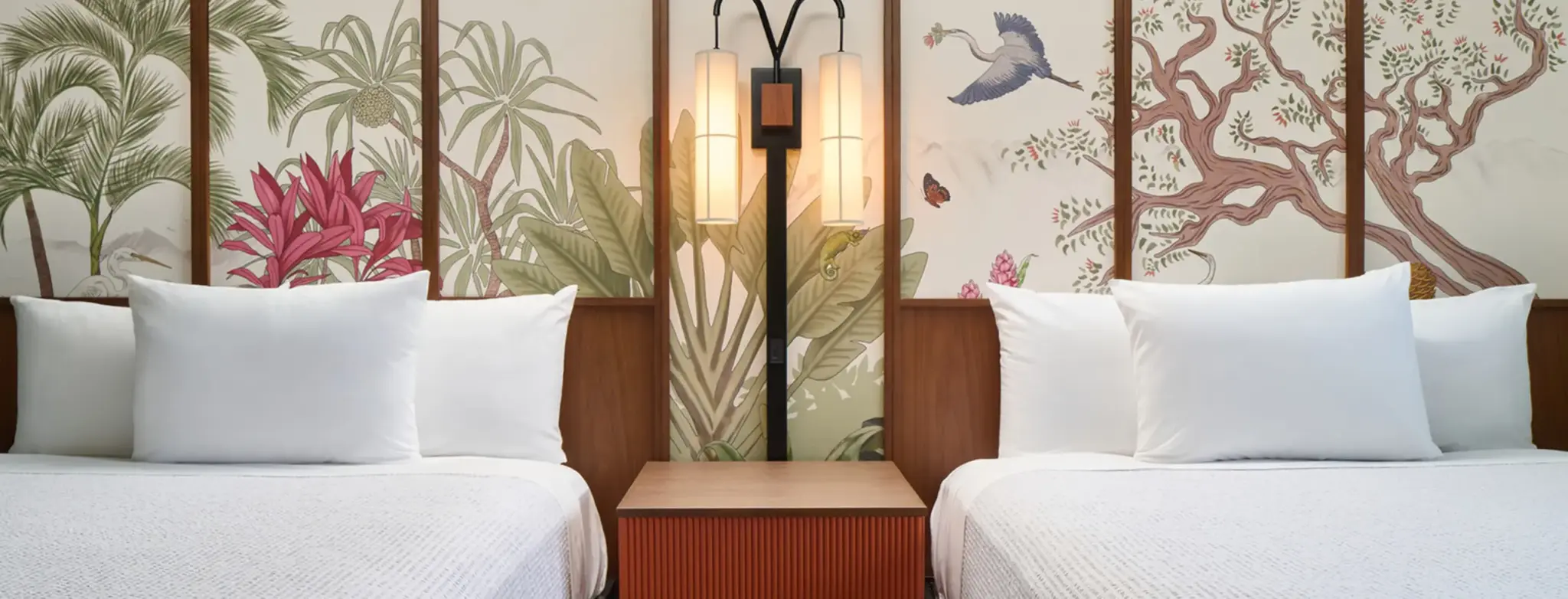 Two beds with white linens against a botanical mural and warm lighting
