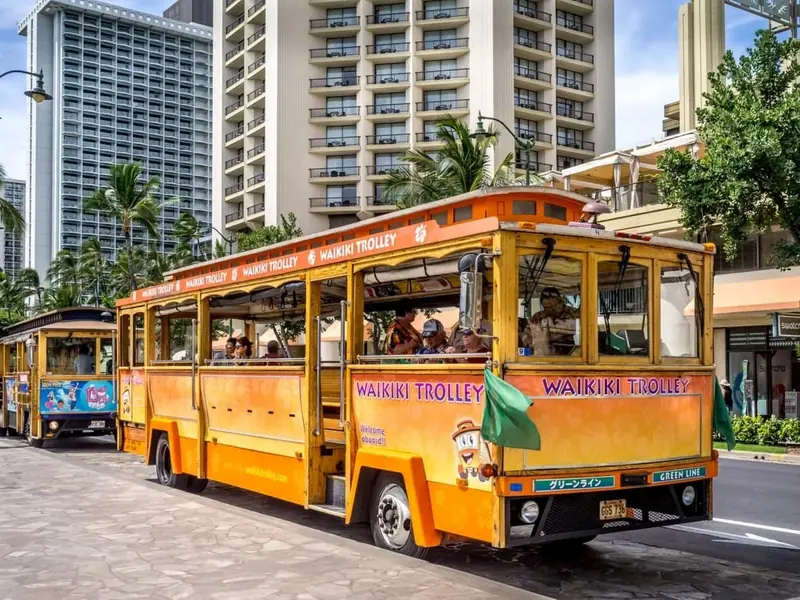 Bright yellow Waikiki Trolley driving past high-rise buildings