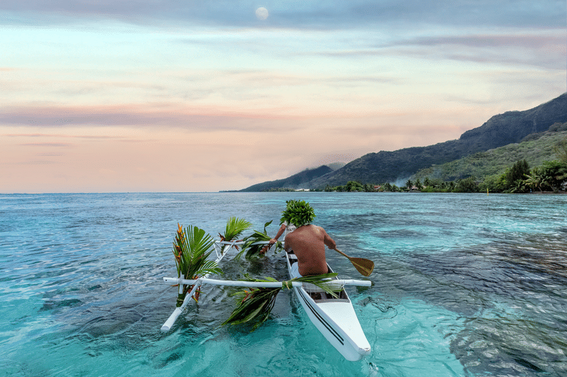 Traditional Hawaiian outrigger canoe on the ocean during sunset in Oʻahu