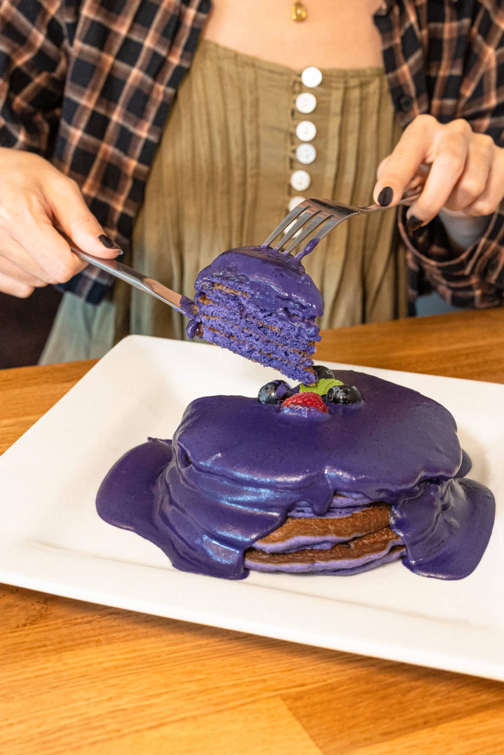 Stack of ube pancakes with purple glaze being cut, topped with berries at Yogur Story Honolulu
