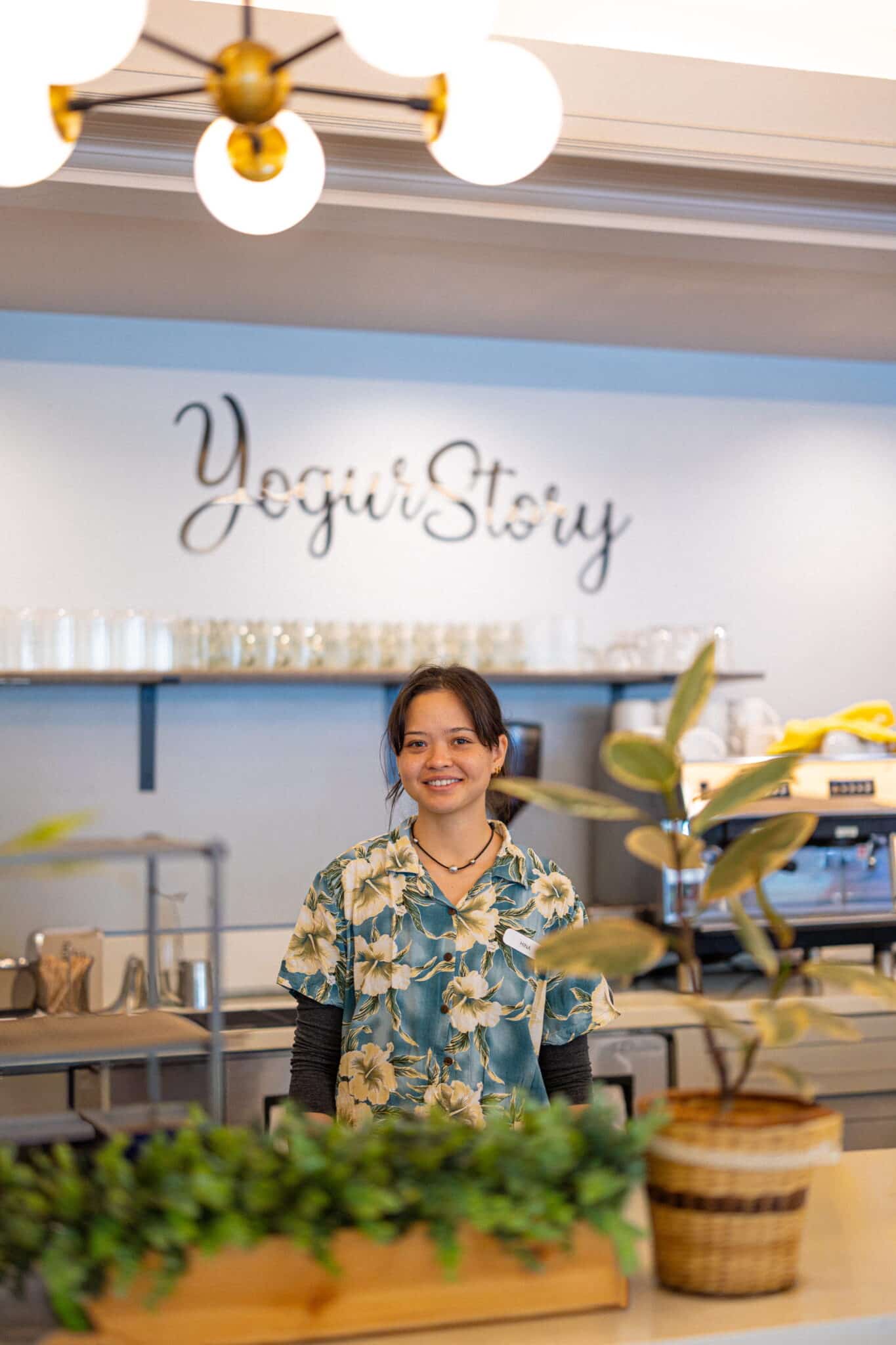 Staff member smiling inside Yogur Story café in Honolulu with restaurant branding in background